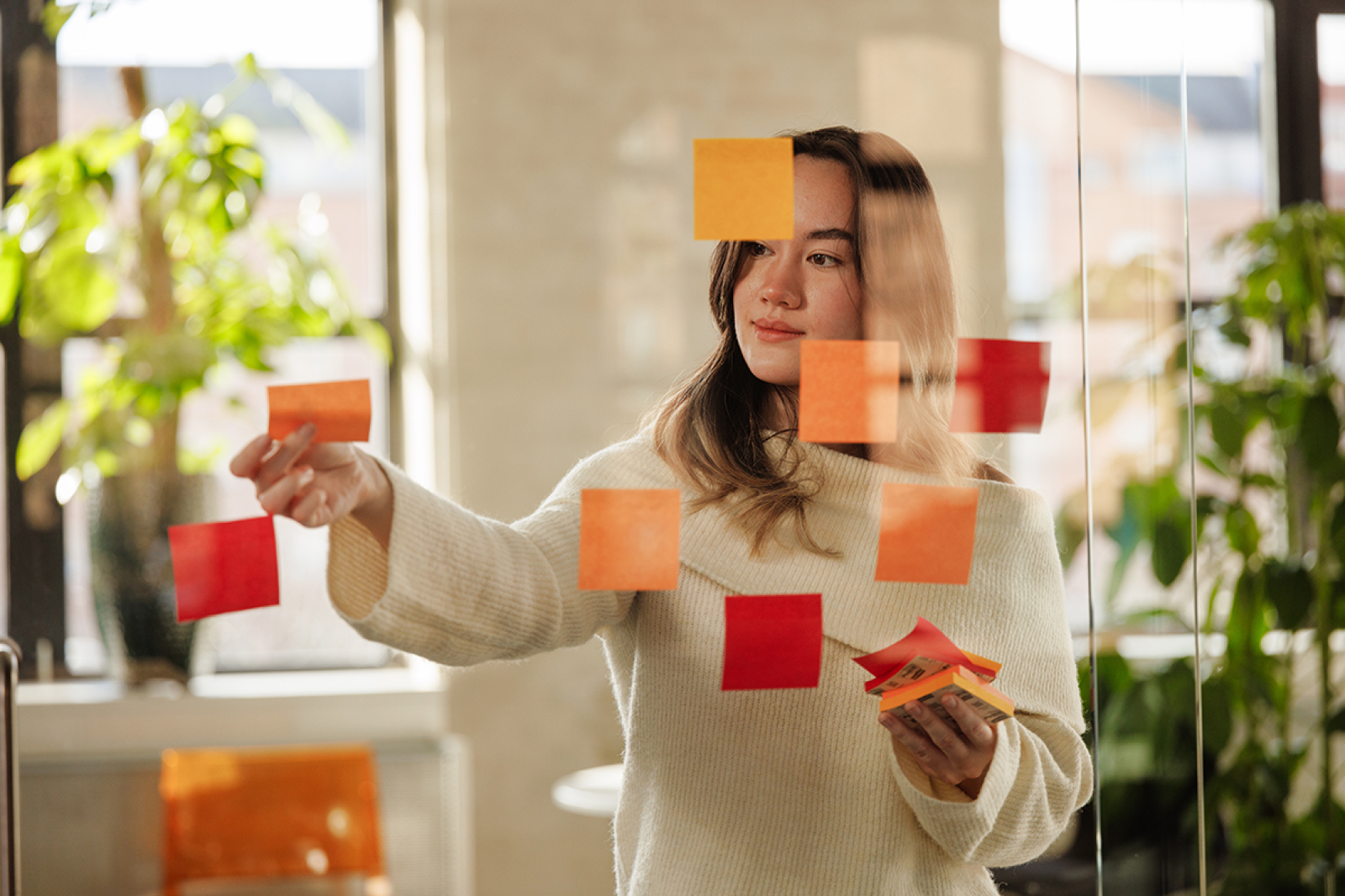 Woman placing a sticky note on a glass wall covered with other colorful sticky notes