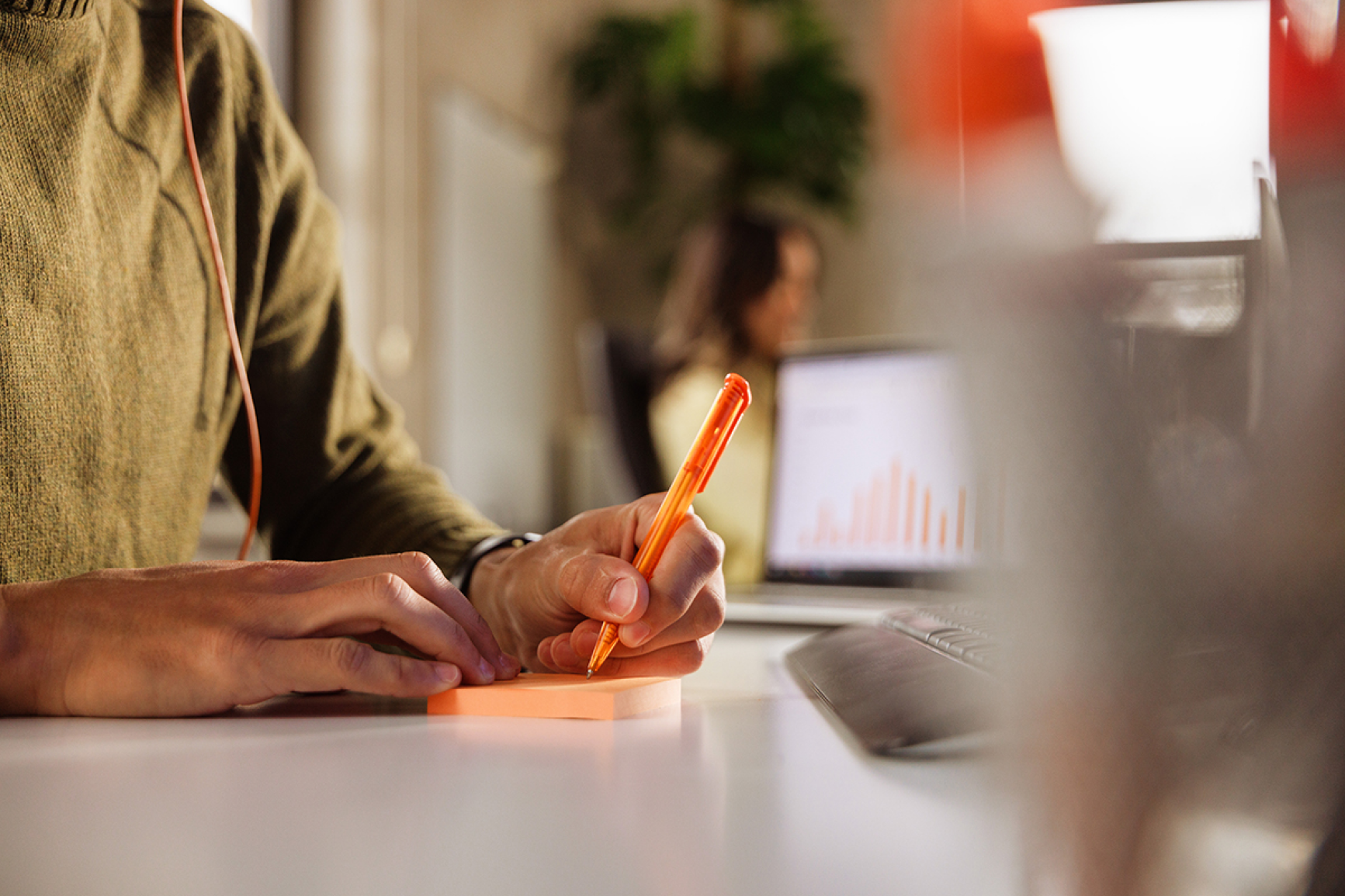 Man sitting at desk taking notes with an orange pen on orange paper